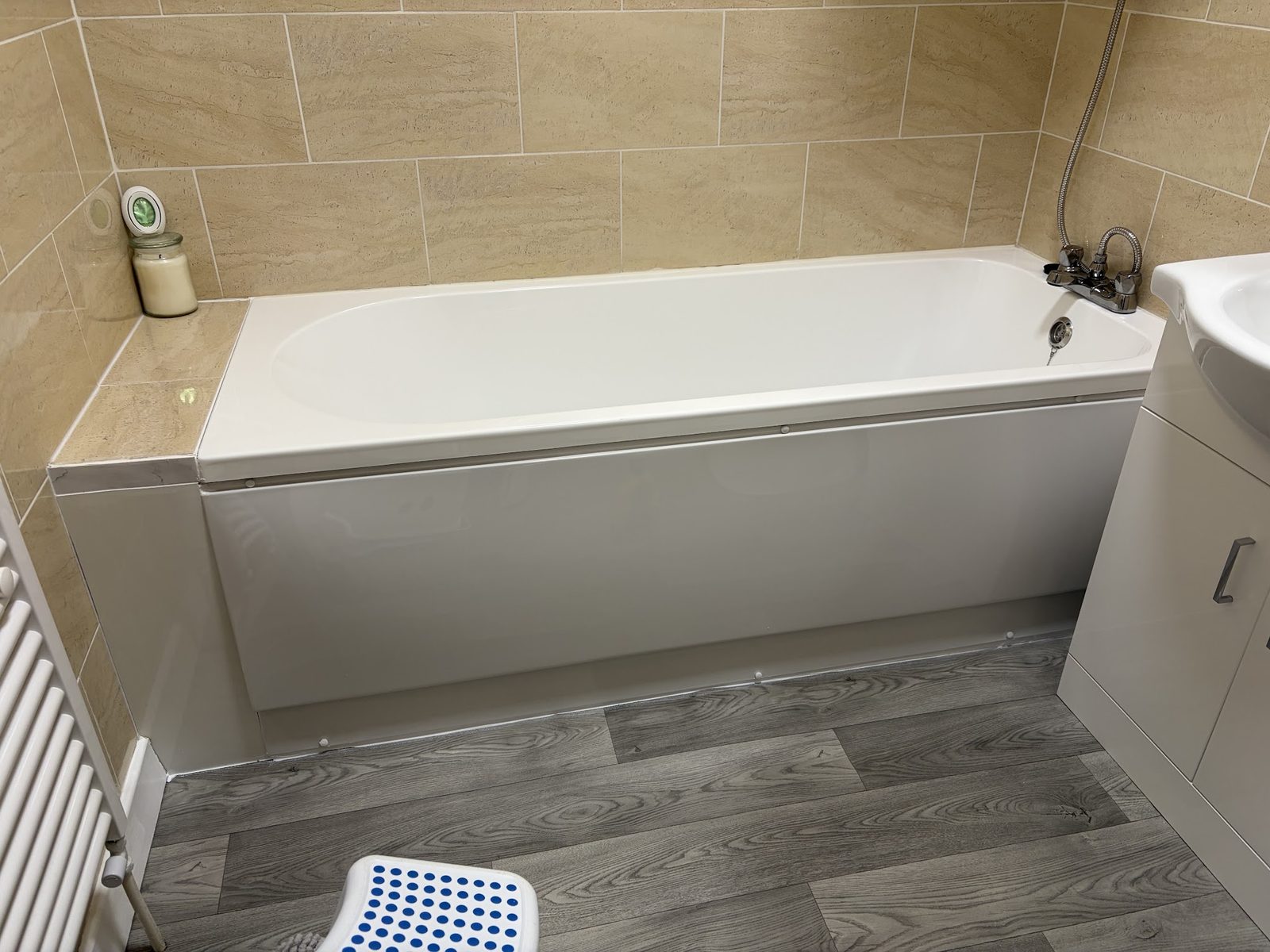 A bath with a tiled surround and a towel radiator beside it